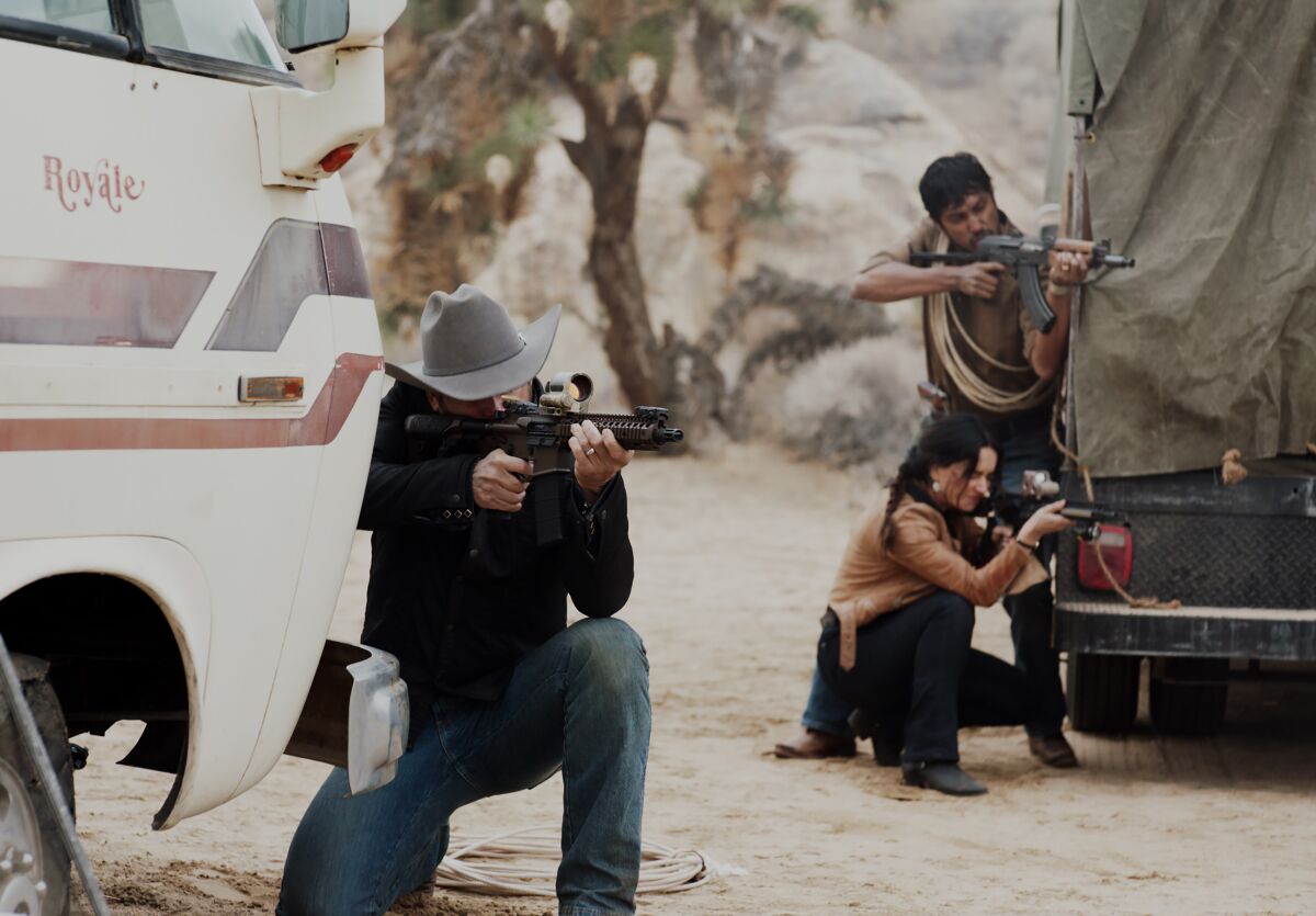 Three people crouch behind vehicles and point guns in the same direction