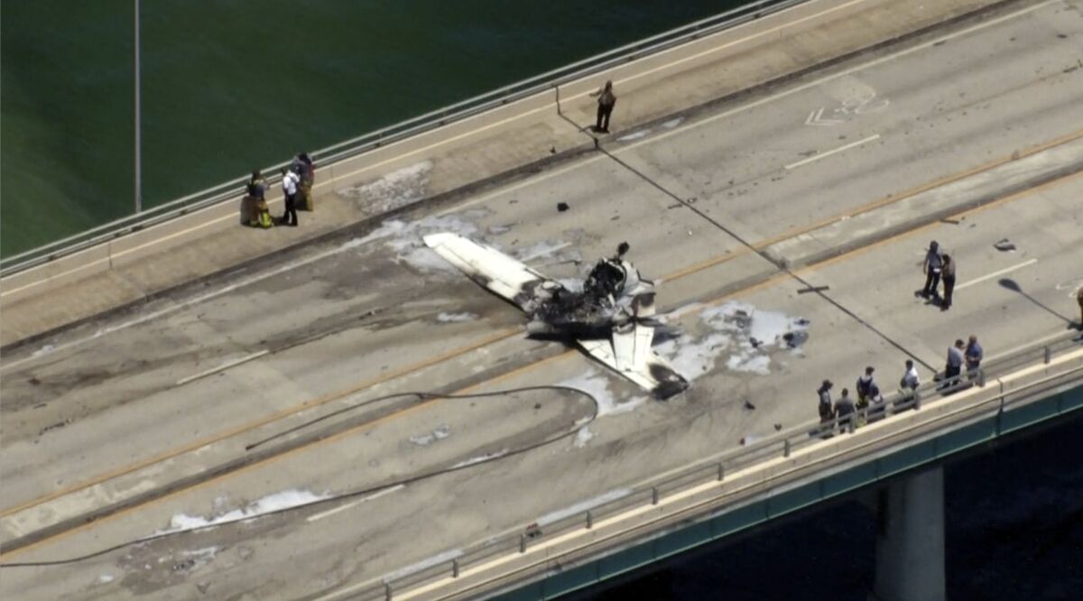 This photo provided by WSVN-TV emergency personnel respond to a small plane crash in Miami on Saturday, May 14, 2022. The small plane has crashed on a bridge near Miami, striking an SUV and bursting into flames. The Federal Aviation Administration reported the single-engine Cessna 172 lost power just before Saturday's crash. (WSVN-TV via AP)