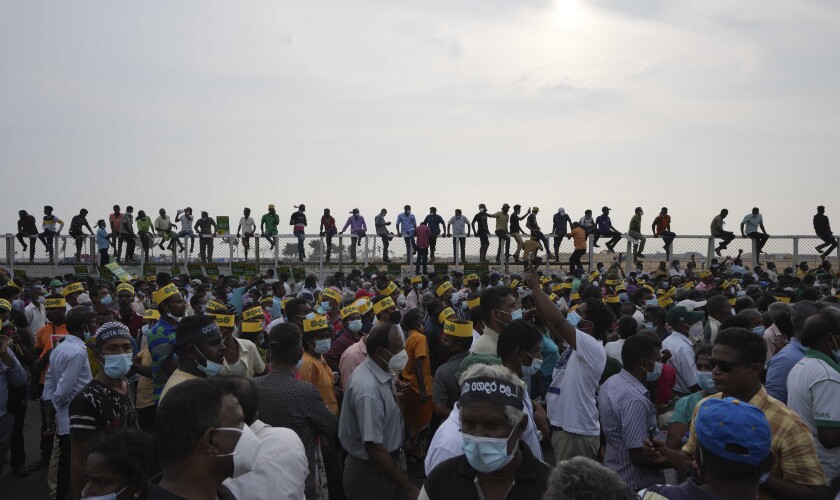 Supporters of Sri Lanka's main opposition sit on the fence of the Chinese owned Port City project as they gather a protest outside the president's office in Colombo, Sri Lanka, Tuesday, March 15, 2022. The protestors were demanding the resignation of President Gotabaya Rajapaksa as the country suffers one of the worst economic crises in history. (AP Photo/Eranga Jayawardena)