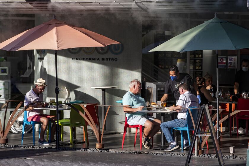 PALM SPRINGS, CA - JULY 16, 2020: A waiter wearing a mask serves customers seated in the outdoor dining area at Lulu's in downtown Palm Springs on July 16, 2020 in Riverside County, California. Riverside County is experiencing a surge in COVID-19 cases.(Gina Ferazzi / Los Angeles Times)