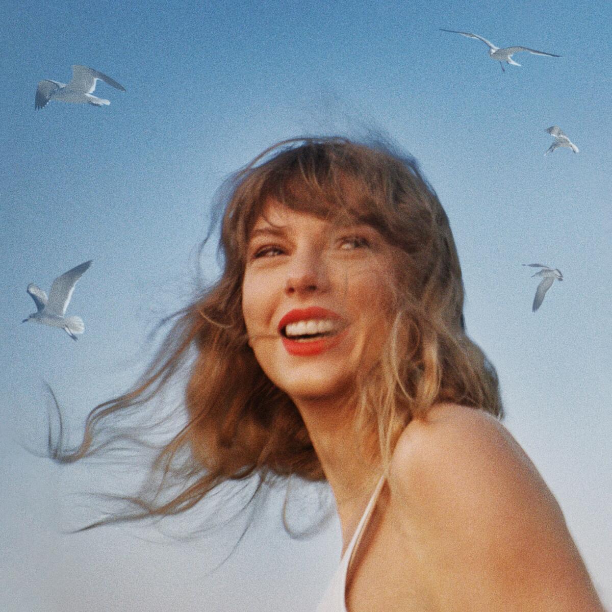 Taylor Swift turns her head and smiles as her hair blows in the wind. Seagulls fly overhead.
