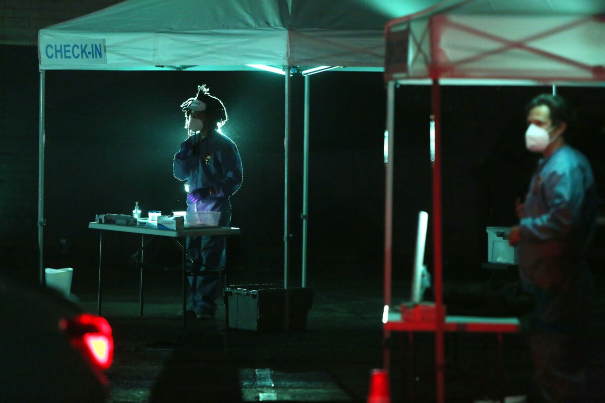 A night-time photo shows actors in protective gear rehearsing a COVID-themed play in a parking lot.