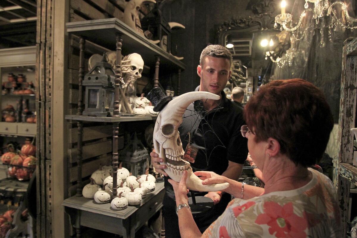 Employee Mick Mulhall, center, helps Josie Carlevato, right, of Chino Hills, take a closer look at a skull moon, by artist Bethany Lowe, during Roger's Gardens' Halloween Boutique Night Gallery on Wednesday.