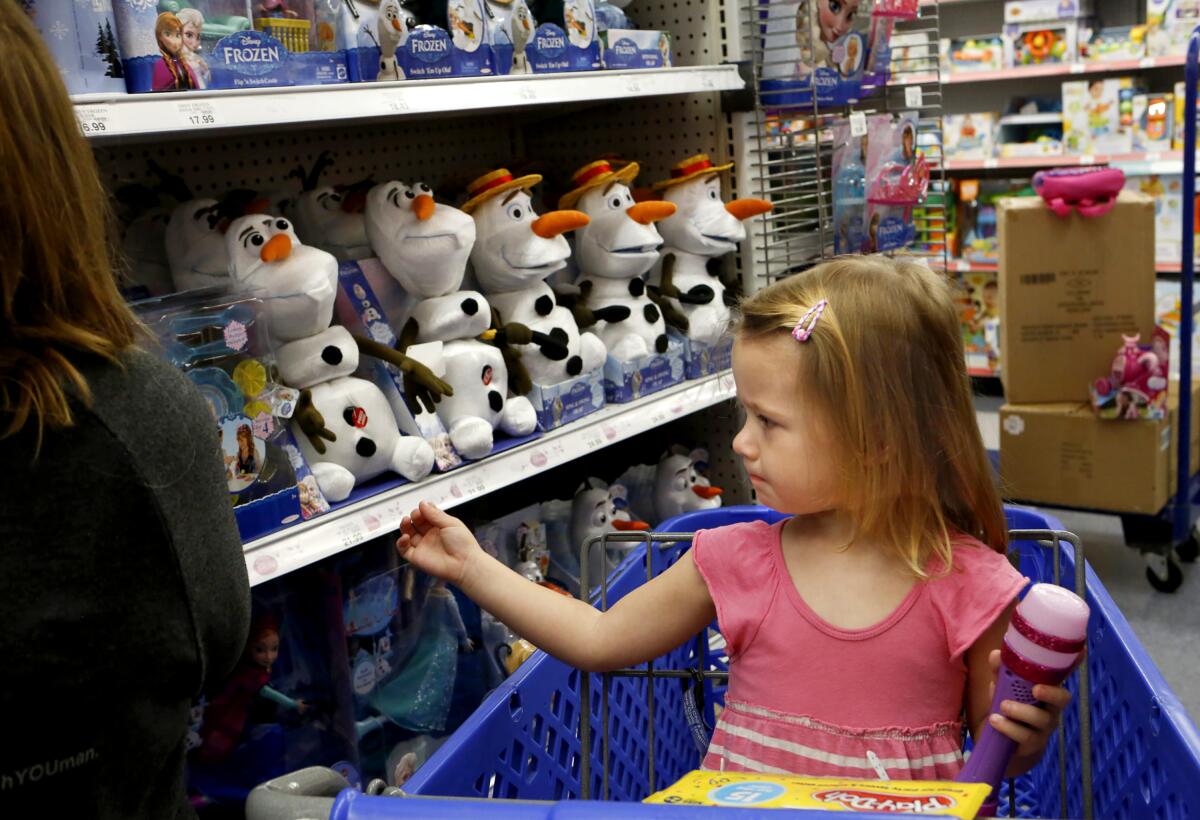 A girl in a shopping cart looks at Olaf toys.