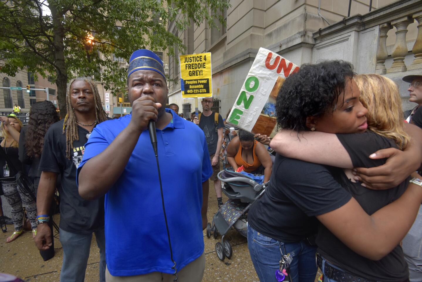 The crowd celebrates the court's decision to try in Baltimore, the cases of six officers charged in Freddie Gray's death and arrest. From left are: Lee Patterson with the Peoples Power Assembly; Rev. Cortly C.D. Witherspoon, with microphone, and Briana Walker hugging Sharon Black, far right.