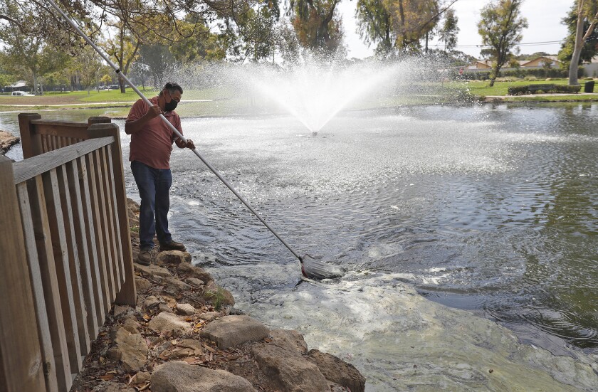A maintenance worker skims debris from one of the two lakes at TeWinkle Park on Monday.