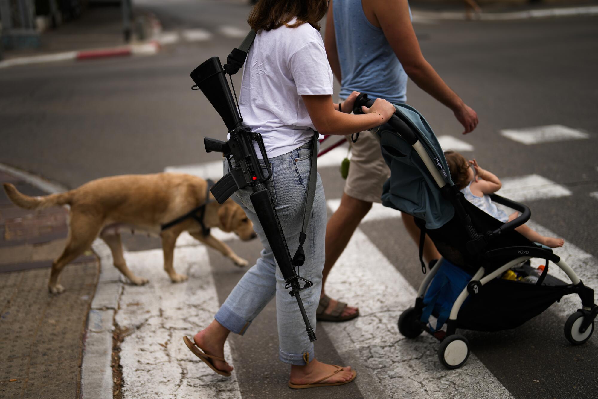 Off-duty Israeli soldier with firearm slung over her shoulder as she pushes a stroller