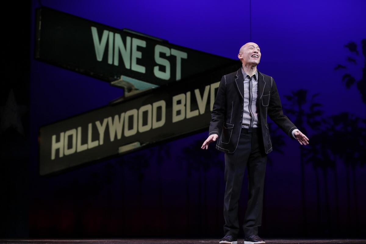 Francis Jue stands on a stage with a Hollywood and Vine street sign projected behind him.