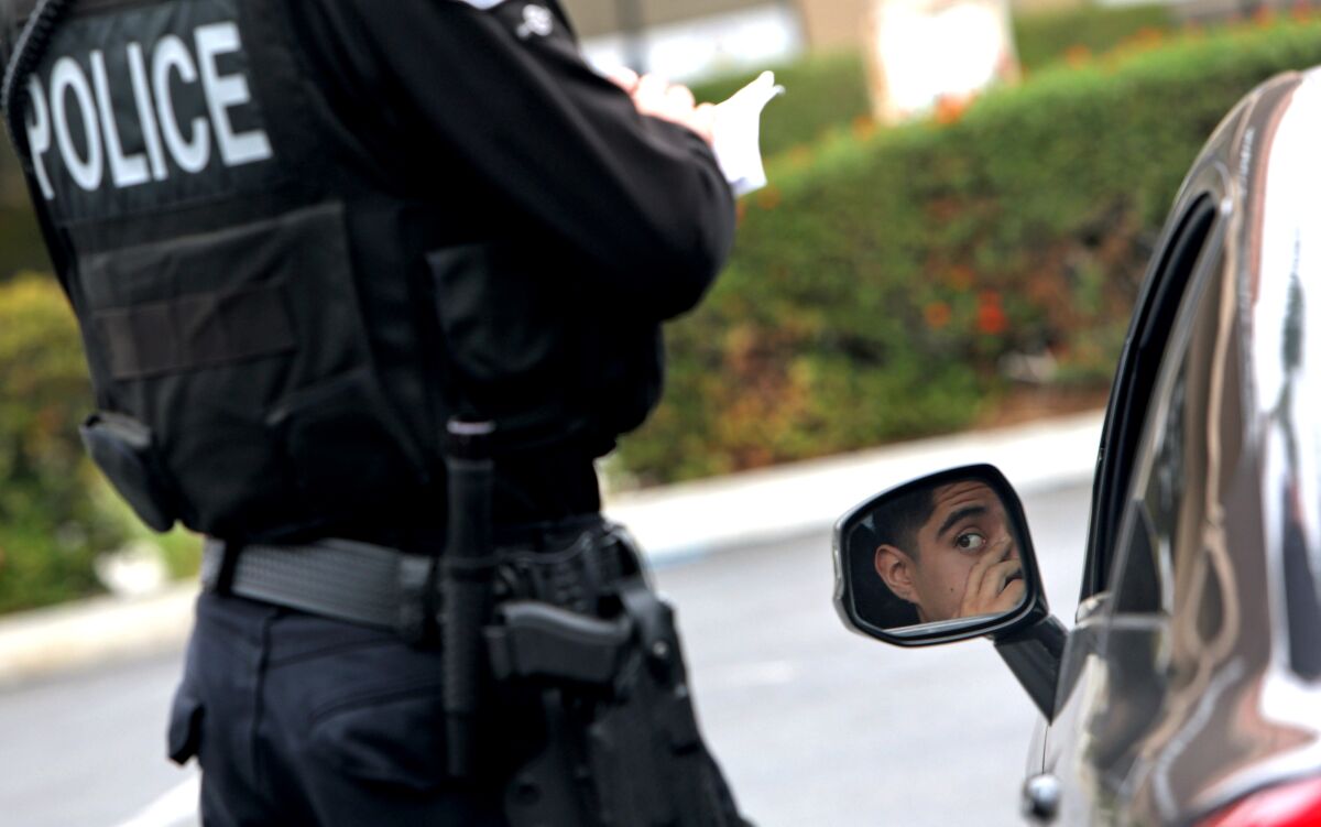 An officer writes a citation standing by a car's rearview mirror with a driver's face reflected in it