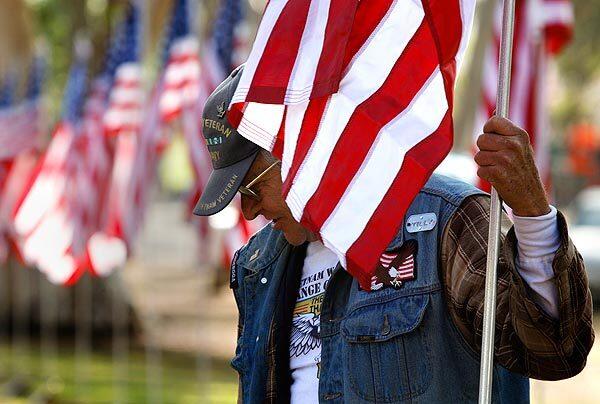 Vietnam veteran David Tilson helps volunteers set up a row of flags at the entrance to the Traveling Vietnam Veterans Memorial at Tri-City Park in Placentia on Wednesday.