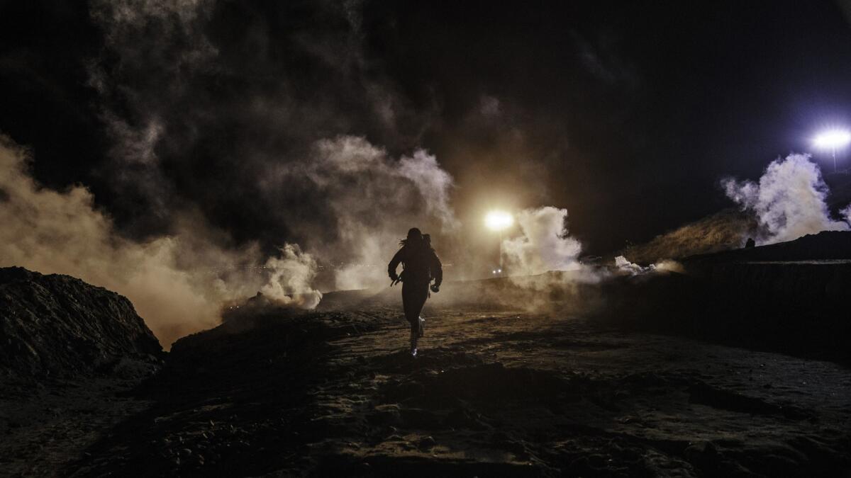 Migrants run as tear gas is thrown by U.S. border officers to the Mexican side of the border fence after the migrants had climbed a fence to try to get to San Diego from Tijuana on Tuesday.