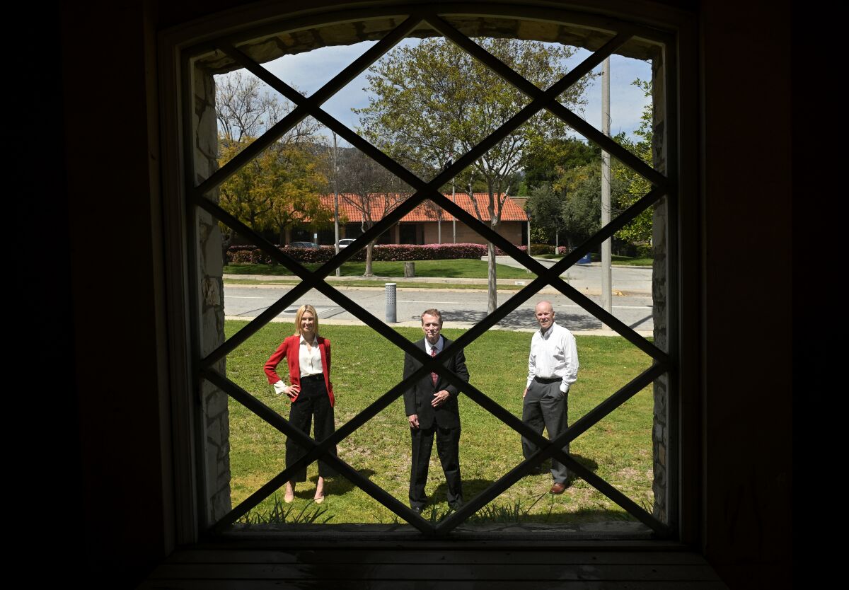 A woman and two men are seen through a window inside a building.