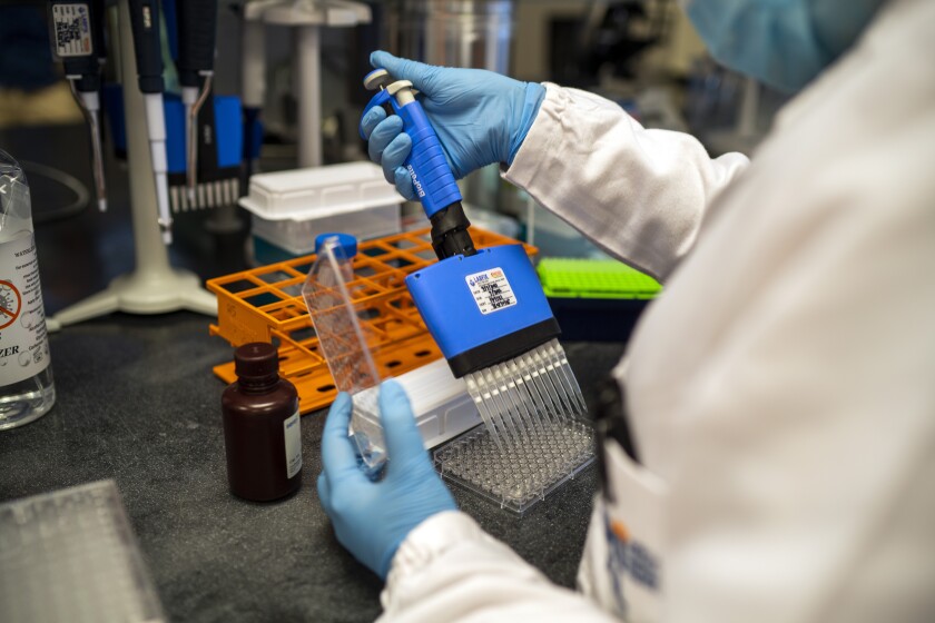 Closeup of the gloved hands of a person in a white coat holding lab equipment.