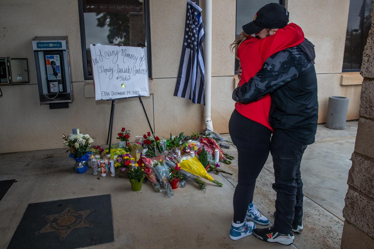 A man and woman hug near a makeshift memorial next to a building.