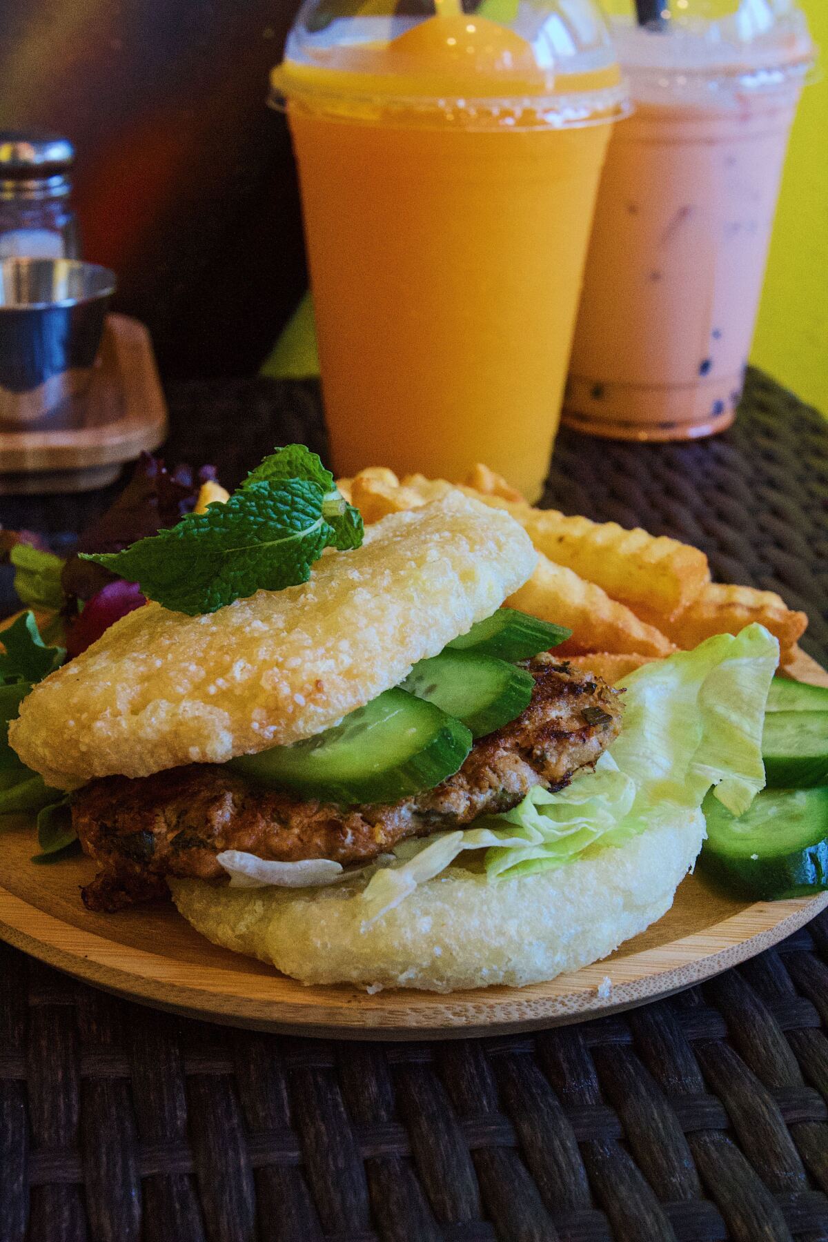 A vertical photo of the larb burger, with rice patties as a bun, from Crazy Thai Burger in Koreatown, plus Thai iced tea