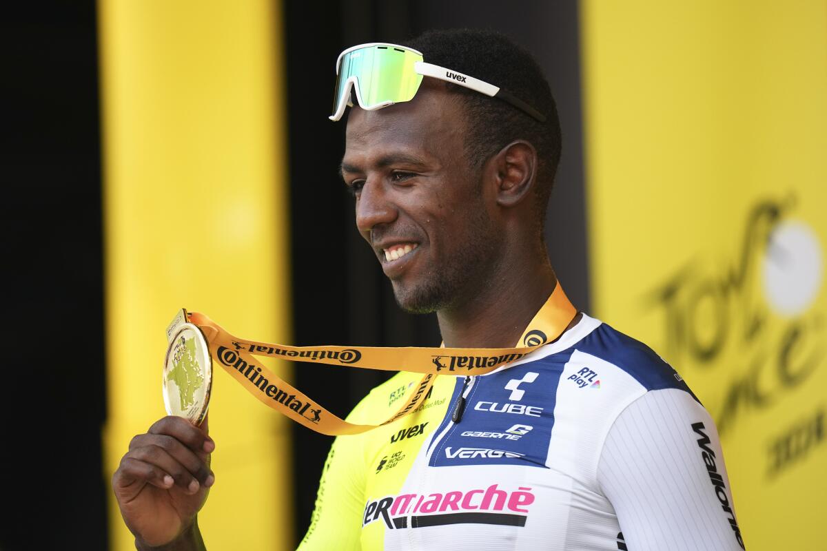 A man with sunglasses on his forehead smiles while looking at a medal he is holding in his hand 