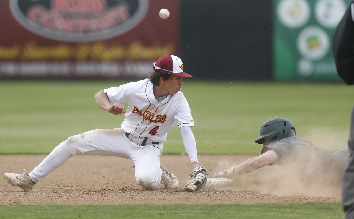 A pickoff attempt skips past Estancia shortstop Jake Humphries (4) as Costa Mesa's Aiden Comte slides in safe at second.