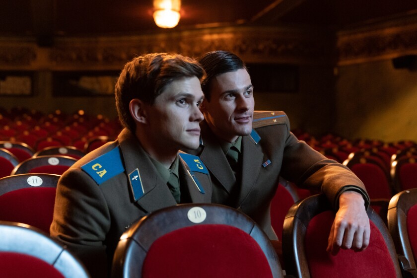 Two men in Soviet military uniforms sit in a theater in a scene from the movie “Firebird.”