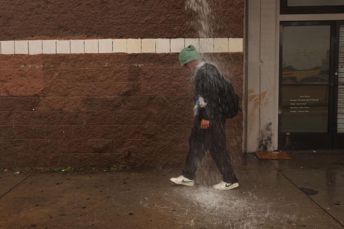 A person walks by as water pours from the top of a building 
