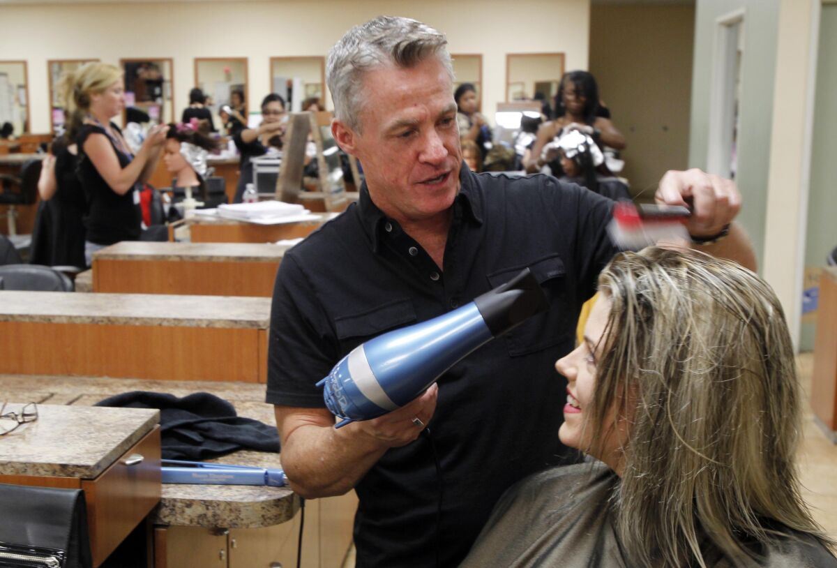 A man blow dries a woman's hair while she is seated