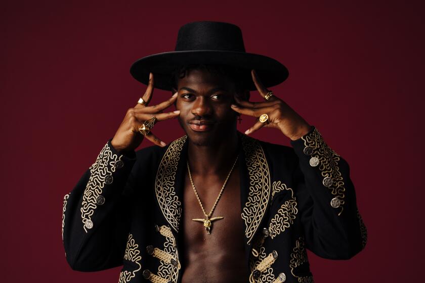 A man poses in front of a red backdrop wearing a black hat