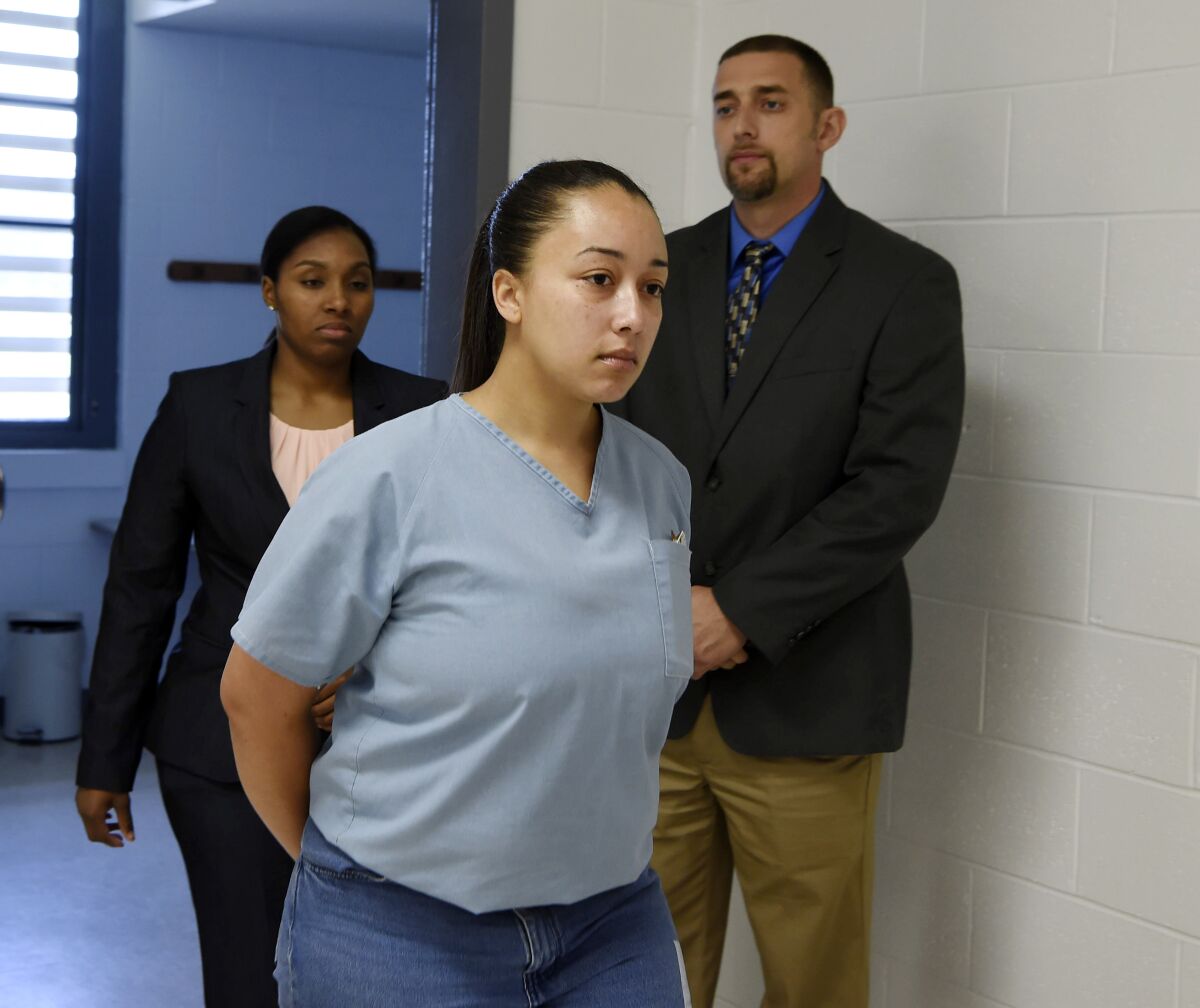 A young woman in handcuffs walks down a hallway