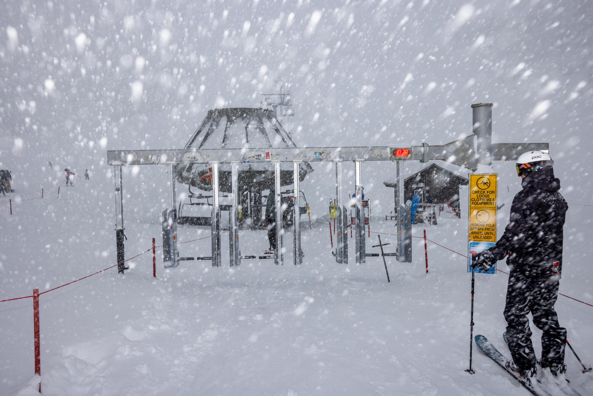 Snow falls as a skier waits to take a ski lift.