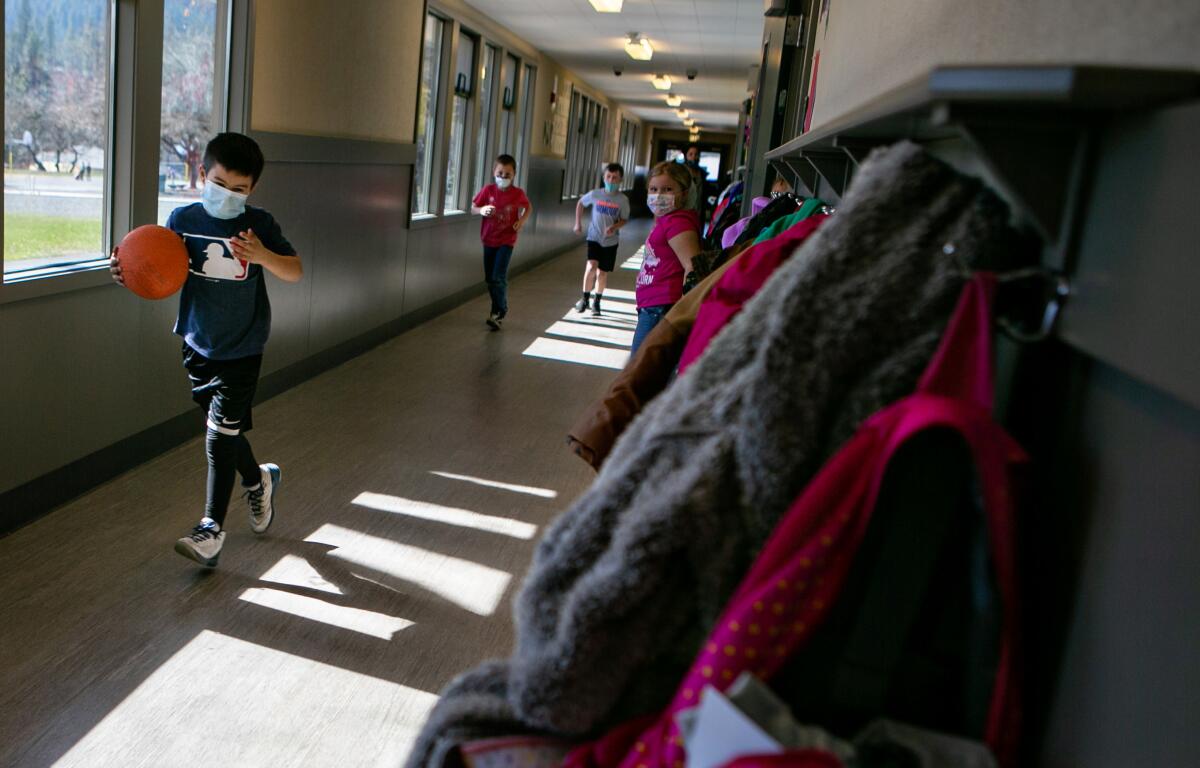 Kids wearing masks run to recess from inside their school.