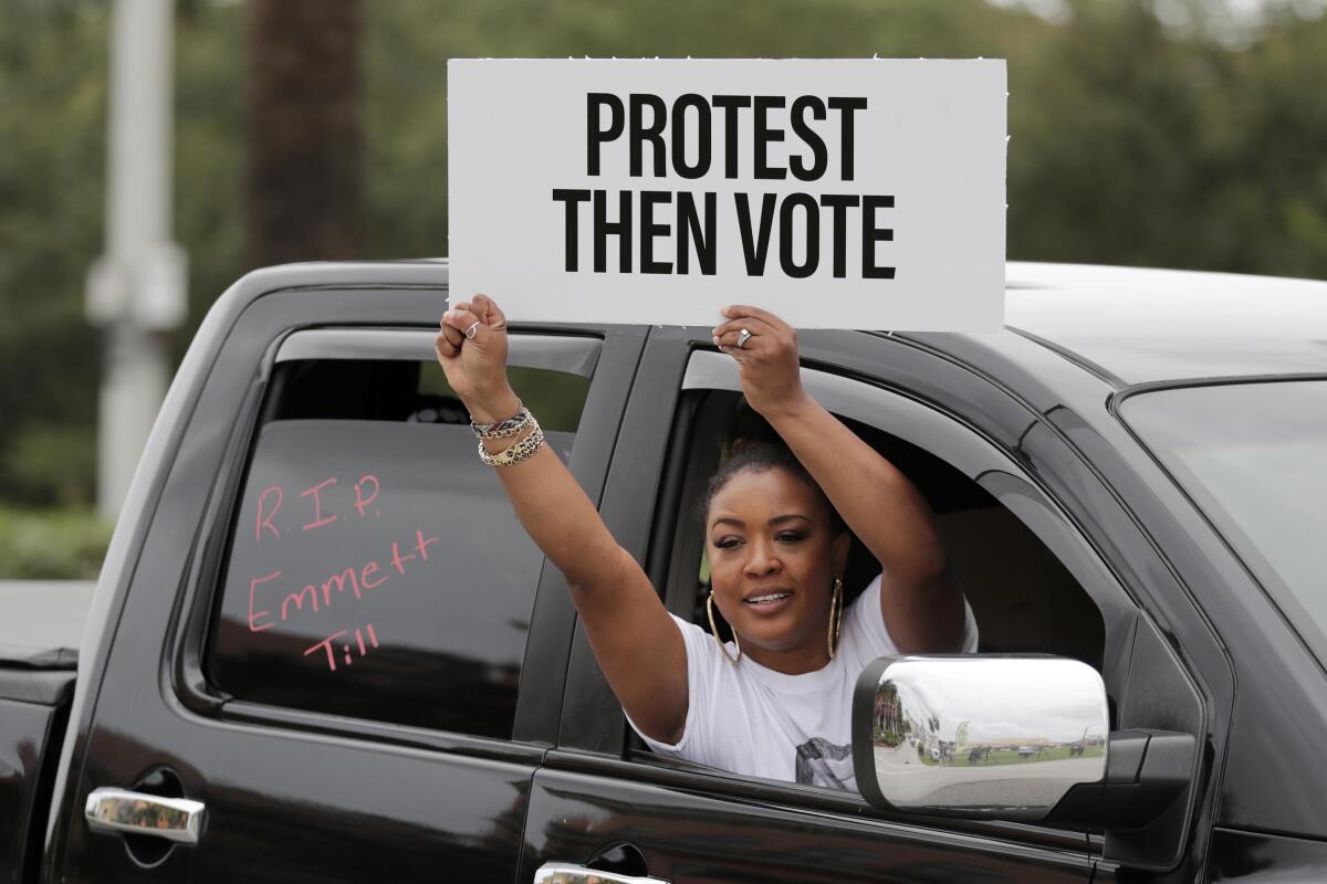 A woman holds a sign saying "Protest Then Vote" during a mock funeral procession in Hallandale Beach, Fla.