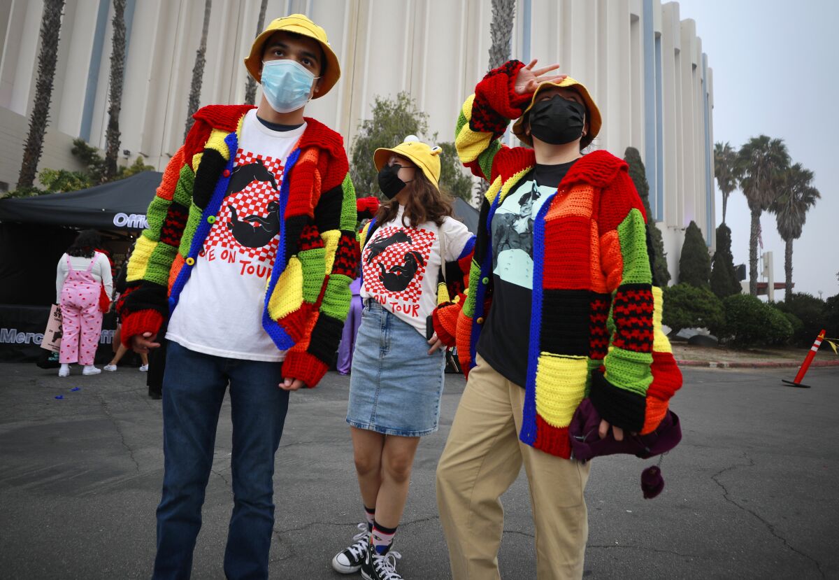 Three people standing in colorful outfits outside a music arena