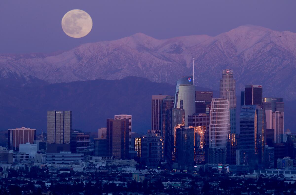 A full moon rises over the snow-capped San Gabriel Mountains and the skyline of downtown Los Angeles 