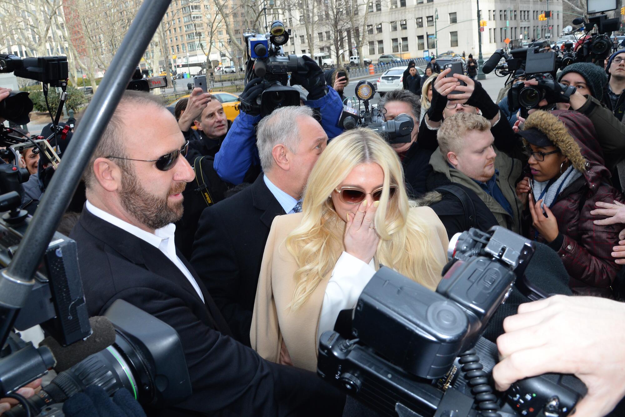 Singer Kesha surrounded by news media outside a courtroom