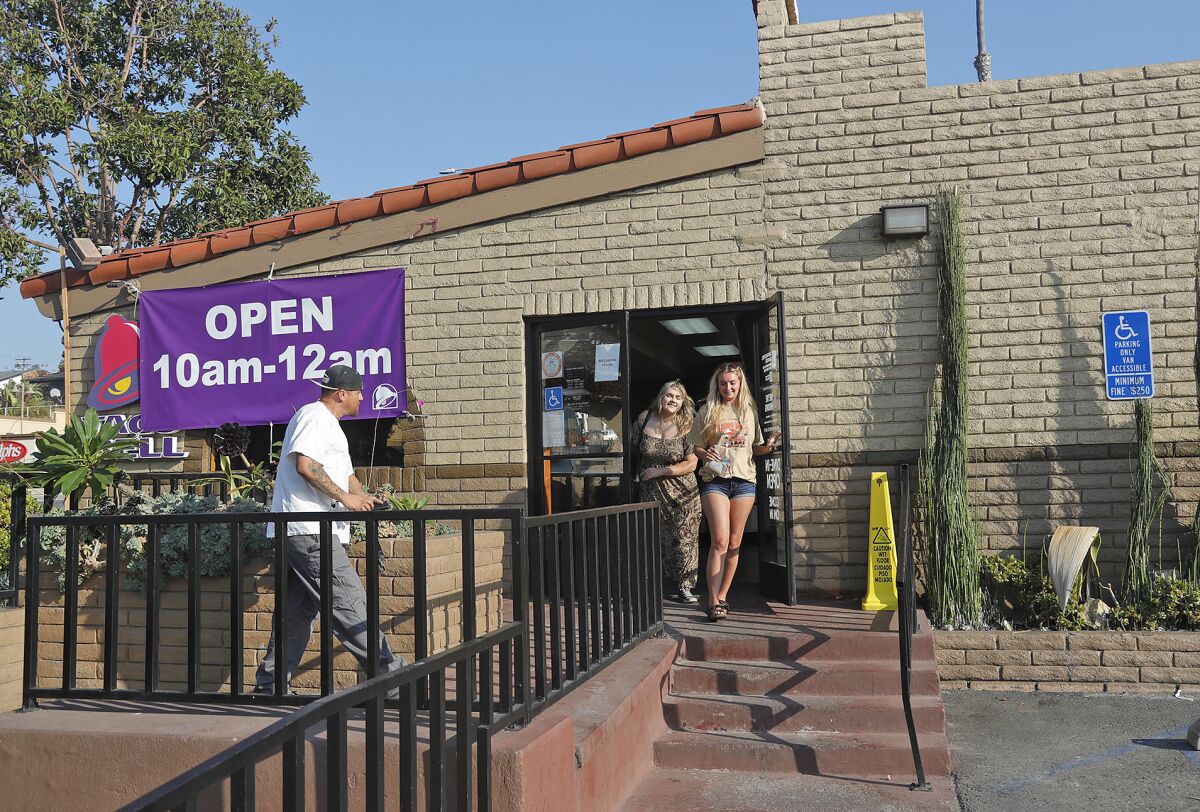 Customers enter and exit a Taco Bell with a red tile roof