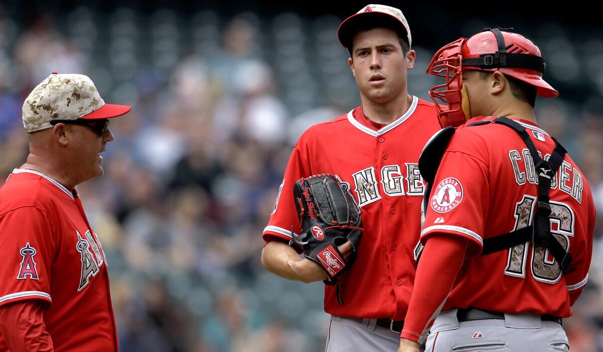 Angels pitching coach Mike Butcher, left, talks to starter Tyler Skaggs and catcher Hank Conger in the second inning Monday in Seattle.