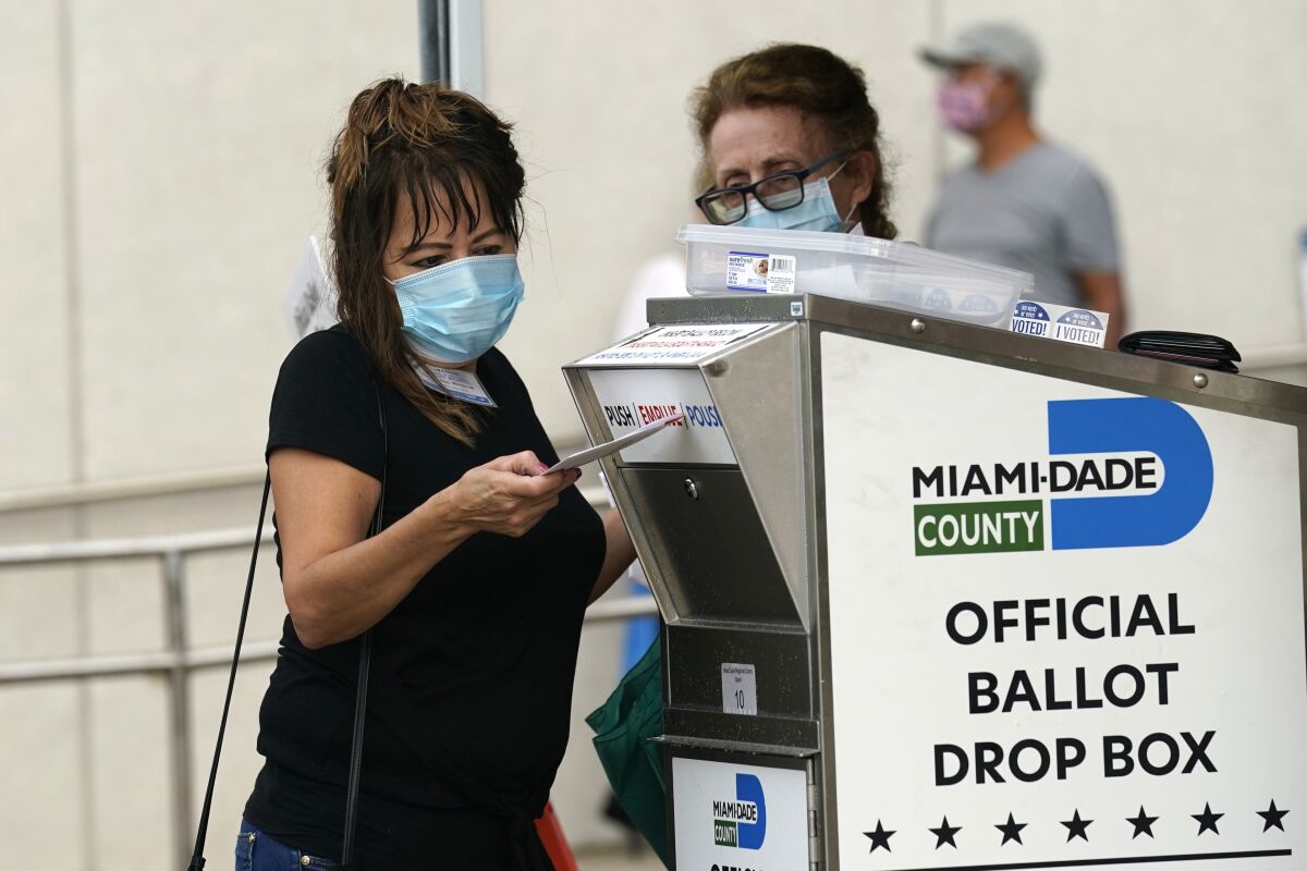 Election worker places mail-in ballot into an official ballot drop box in Miami.