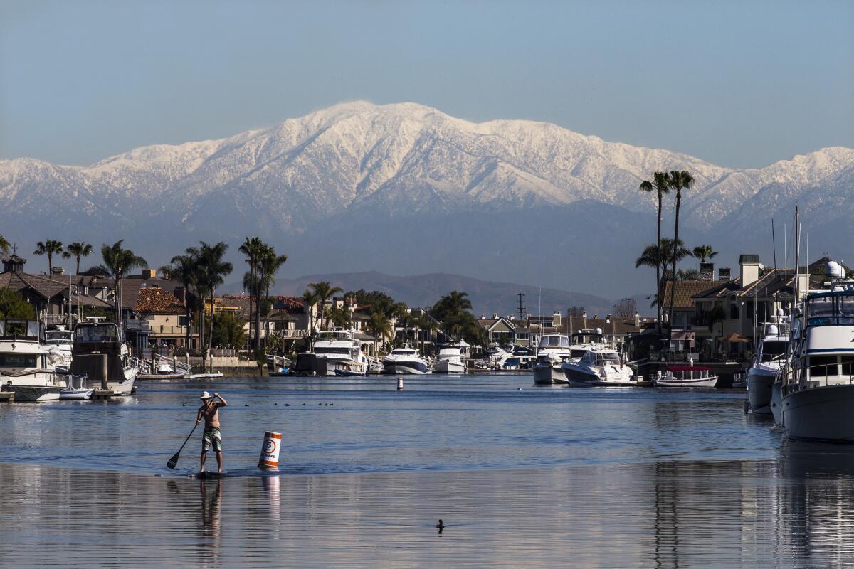 Amid warm temperatures, stand-up-paddle boarder David Molesky, of Brooklyn, N.Y., paddles through Huntington Harbor with a scenic view of the recently snow-capped San Gabriel Mountains on Feb. 24.
