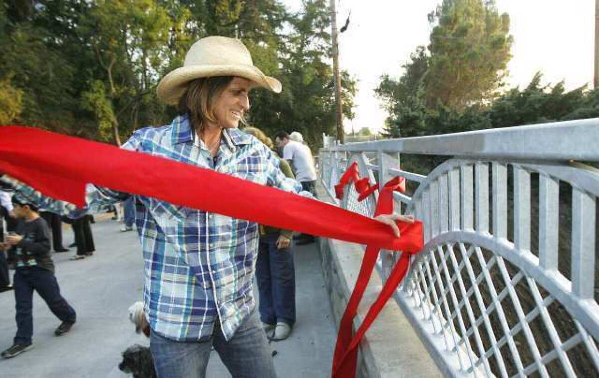Julie Thurston, who lives near the Jessen Bridge, threads the red ribbon that was cut during the ribbon-cutting ceremony for the bridge into the safety rail as a decoration.
