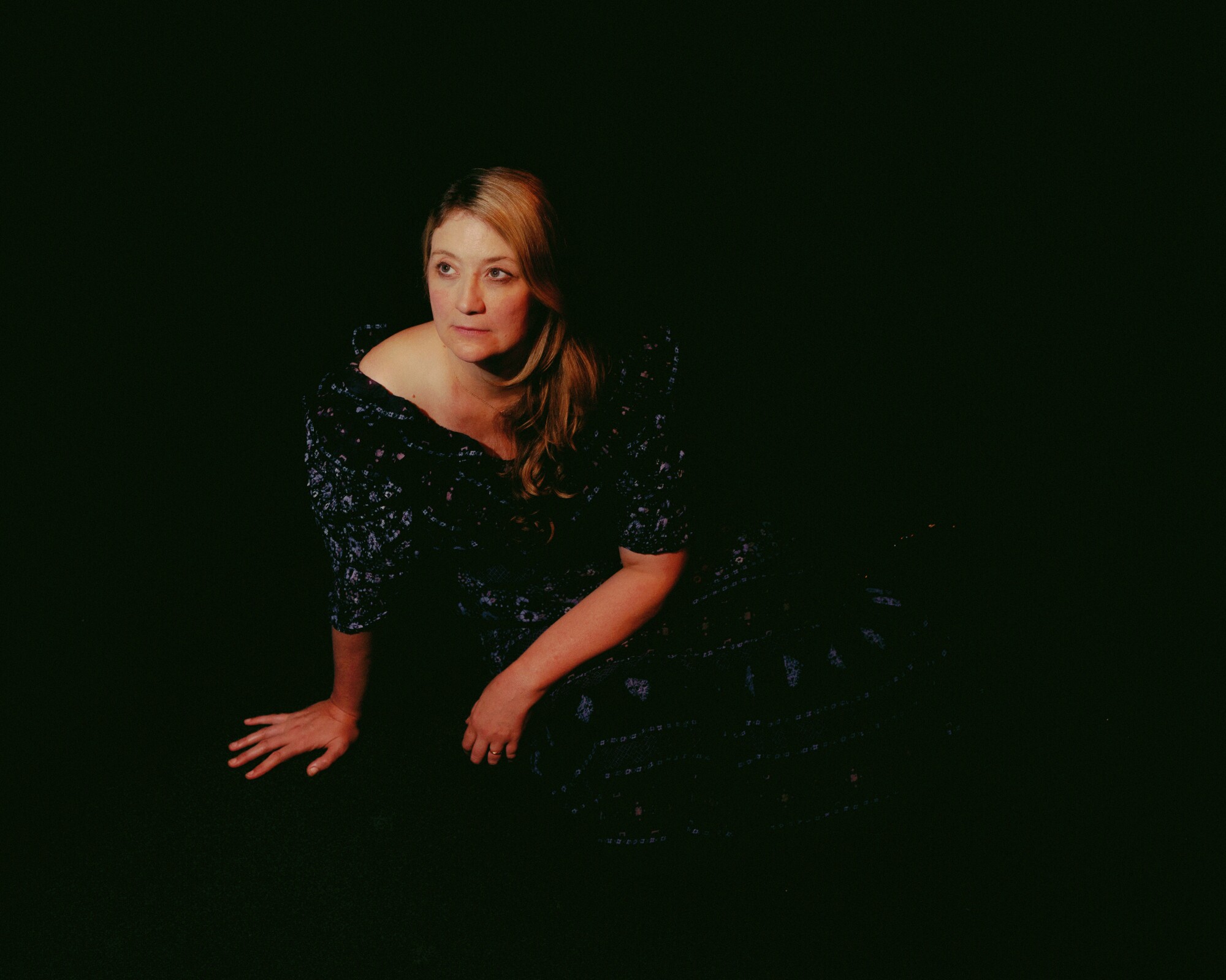A woman in a dress sits on the ground in darkness.