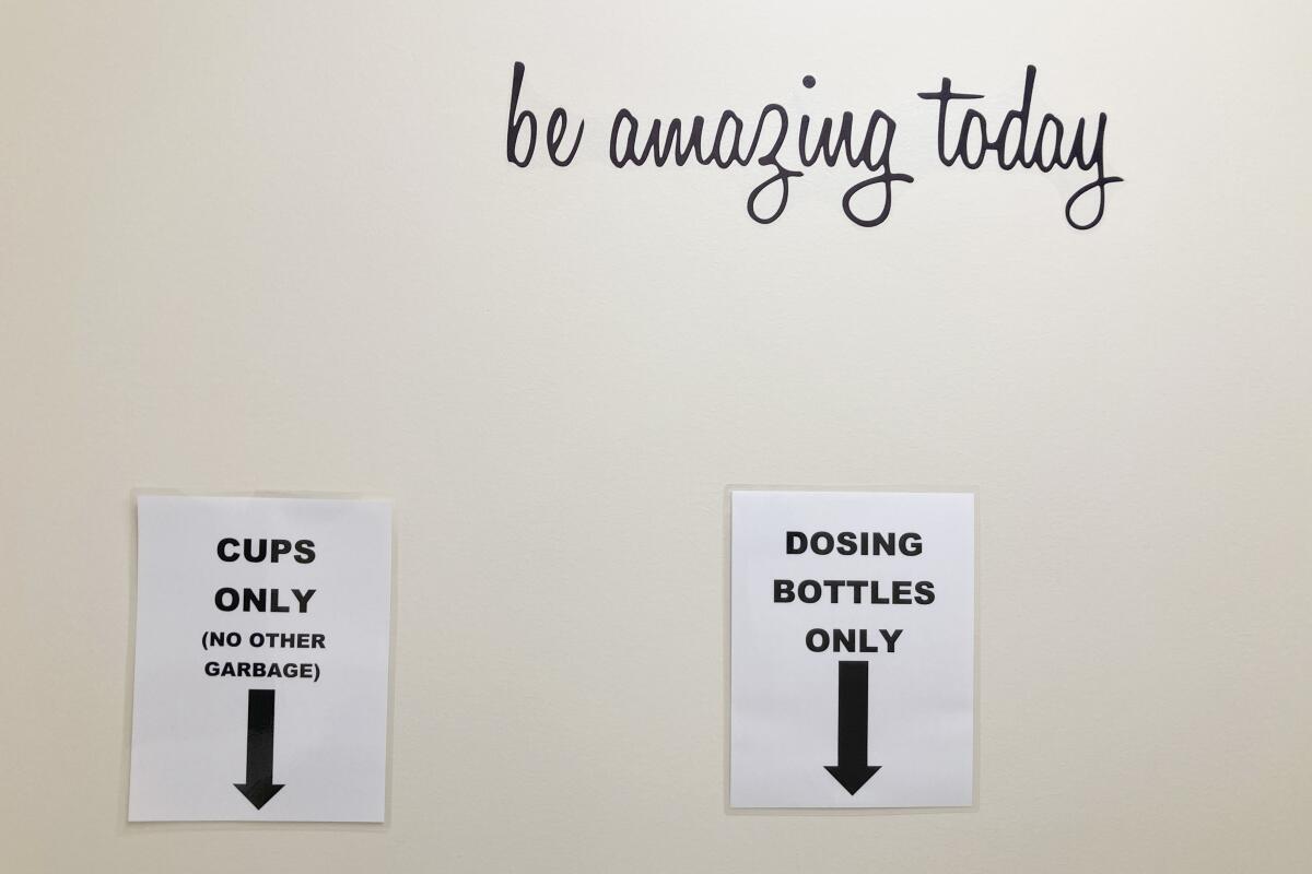 A wall with signs pointing to disposal for cups and dosing bottles 