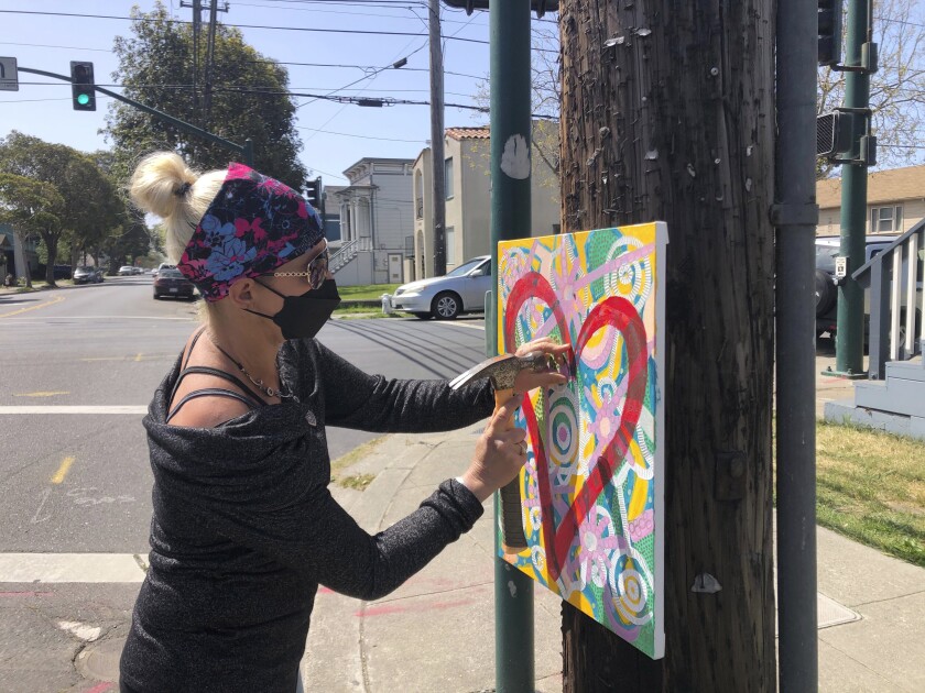 Artist Deirdre Freeman hangs her artwork on a telephone pole in Alameda, Calif., Tuesday, April 13, 2021. Freeman, who has hung over 120 pieces of artwork on telephone poles to spread joy to others, says, "It's starting a love and kindness movement, which is what we need." (AP Photo/Janie McCauley)
