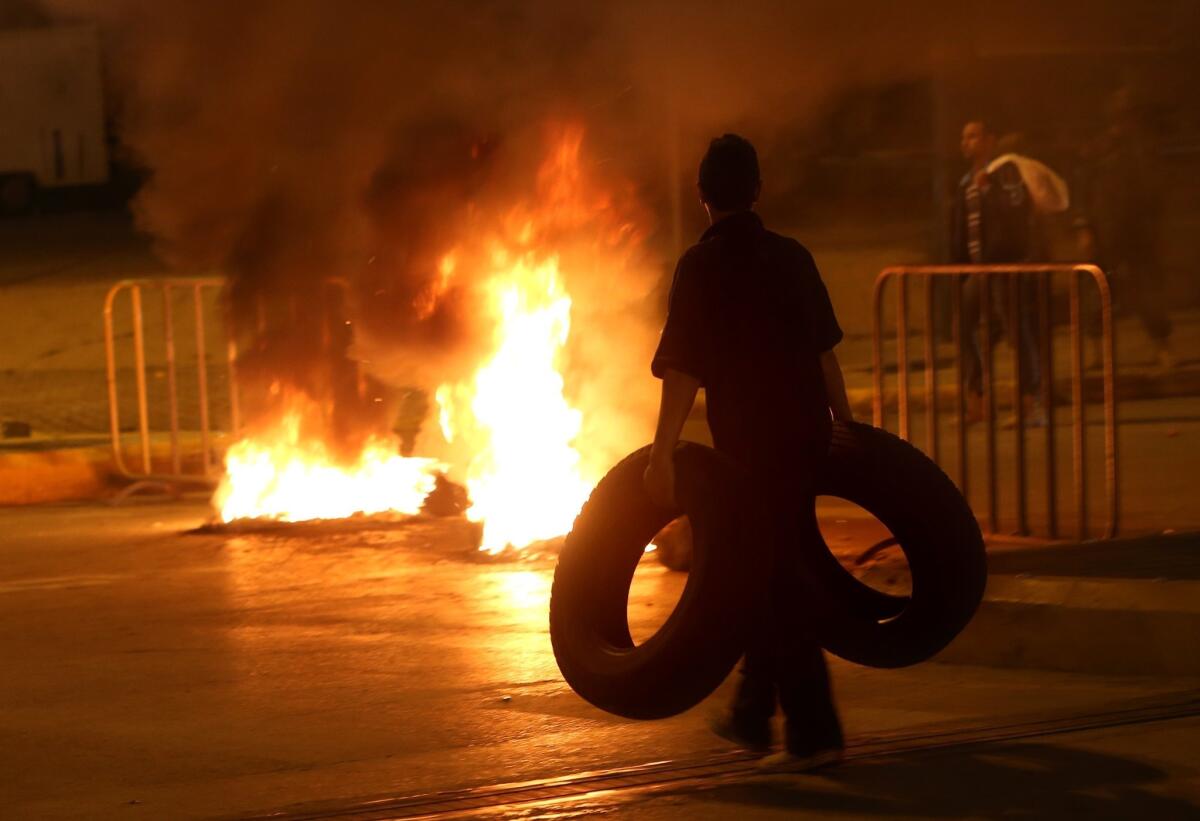 A Sunni protester carries tires as a fire burns on a major roadway between Beirut and the capital's southern suburbs, a Hezbollah stronghold.