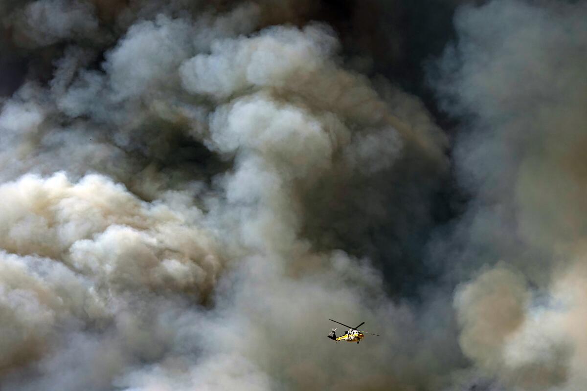 A helicopter flies against roiling black and gray smoke clouds 