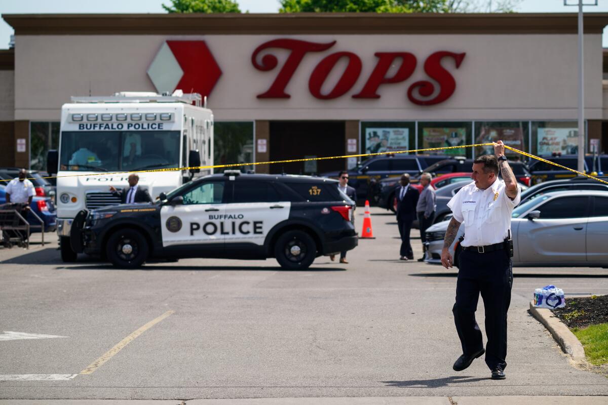 A police officer lifts crime scene tape on the lot of Tops supermarket in Buffalo, N.Y.