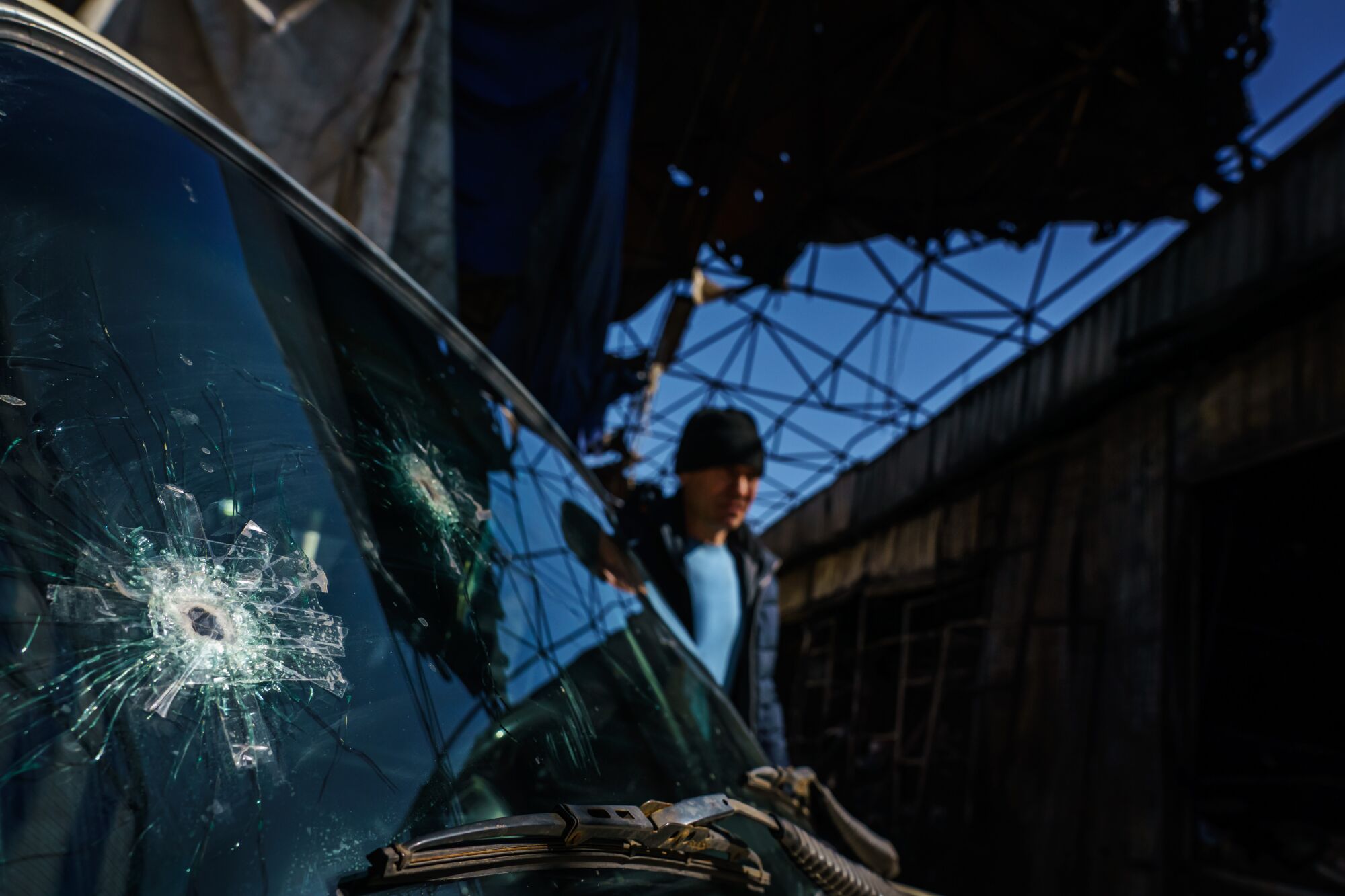 A man walks by a car with bullet holes in its windshield.