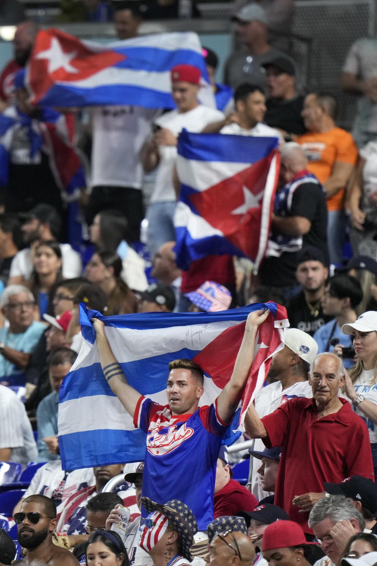 A crowd of soccer fans holding up the flag of Cuba, which a single star in a red triangle against blue and white stripes