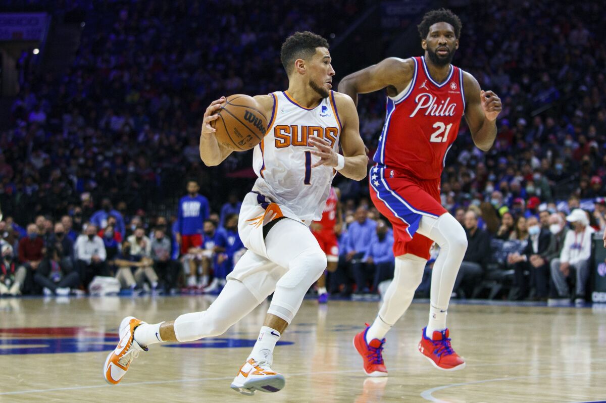 Phoenix Suns' Devin Booker, left, drives to the basket against Philadelphia 76ers' Joel Embiid, right, during the second half of an NBA basketball game, Tuesday, Feb. 8, 2022, in Philadelphia. The Suns won 114-109. (AP Photo/Chris Szagola)