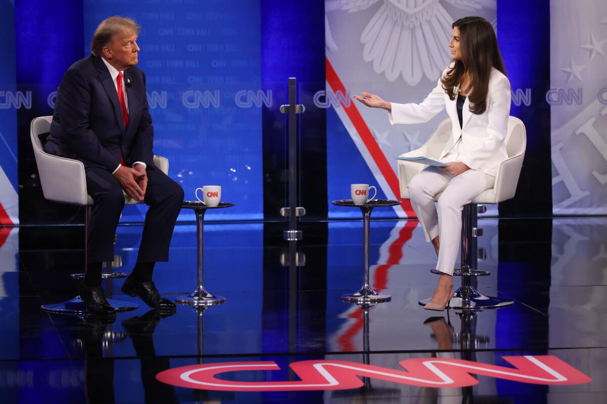 Donald Trump, seated, is questioned by CNN's Kaitlan Collins in a televised town hall, with a big CNN logo on the floor