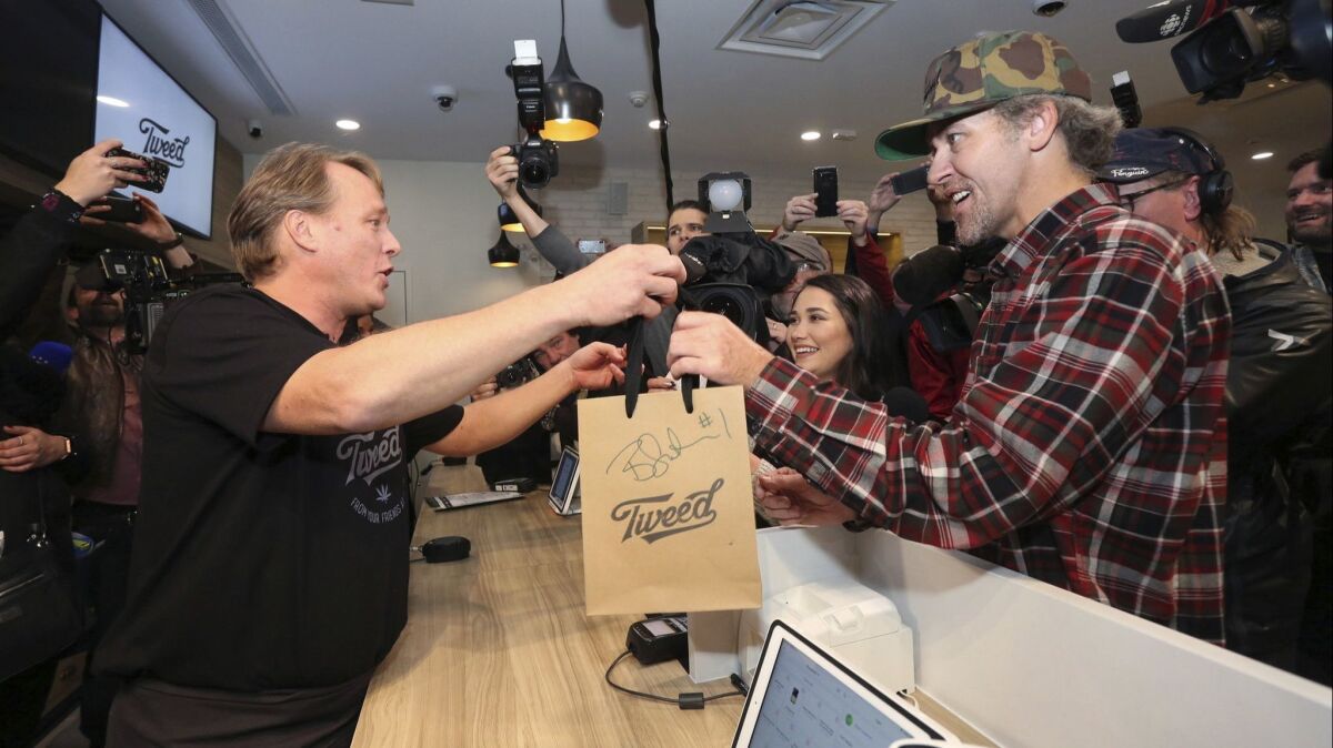 Canopy Growth CEO Bruce Linton, left, passes a bag with the first legal cannabis for recreational use sold in Canada to Nikki Rose and Ian Power at the Tweed shop on Water Street in St. John's, Newfoundland, at 12:01 a.m. on Oct. 17, 2018.