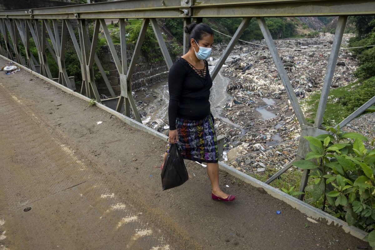 A woman walks over Las Vacas river bridge in Chinautla, on the outskirts of Guatemala City, Wednesday, June 8, 2022. The Ocean Cleanup NGO is currently piloting a trash collection device in one of the world's most polluted rivers, the Las Vacas river, where unique seasonal challenges include huge quantities of waste and massive water pressure during the rainy season. (AP Photo/Moises Castillo)