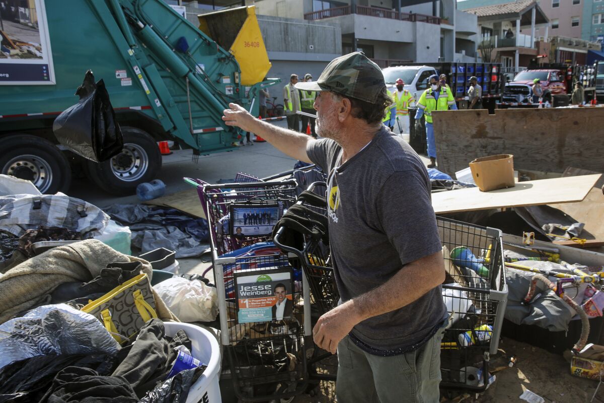 A man surrounded by his belongings gestures to a garbage truck